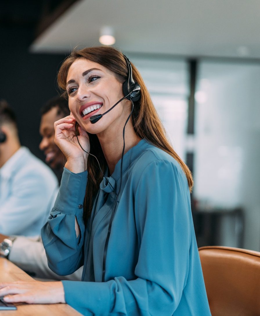 Imagem ilustrativa: atendente com headset sorri sentada à mesa de trabalho