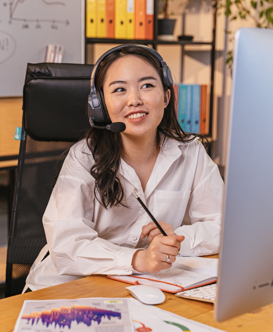 Imagem ilustrativa: atendente com headset sorri sentada à mesa de trabalho