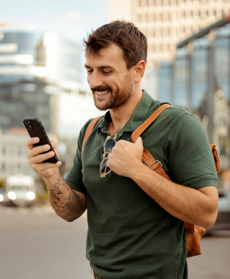 Imagem ilustrativa: homem sorri usando o celular na rua, na cidade